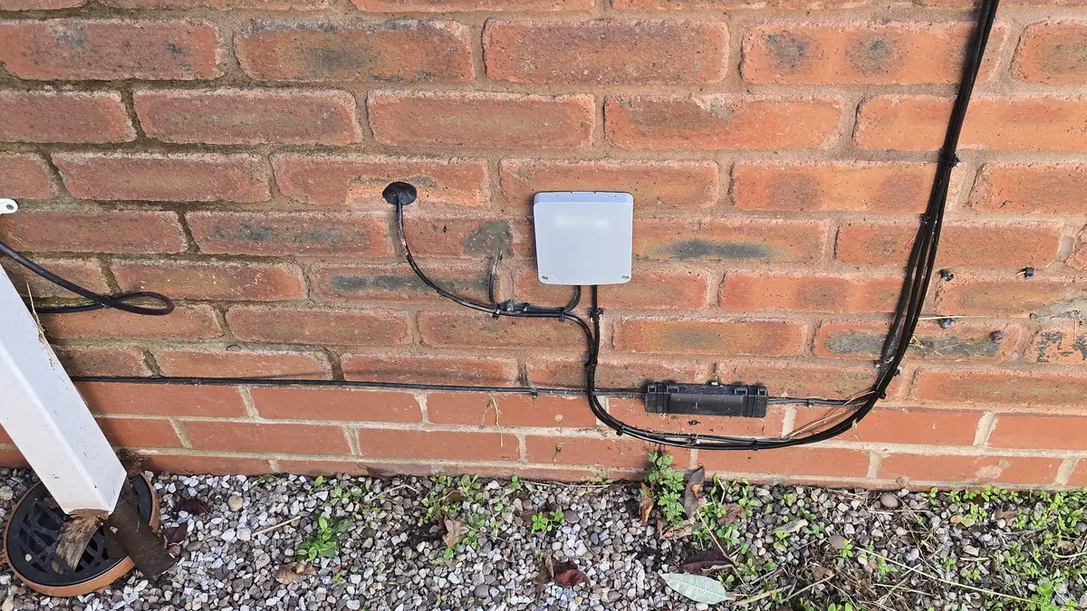 An Openreach external junction box on a red brick wall, with the drilled fibre entry point to its left and the drop cable clipped along the brickwork